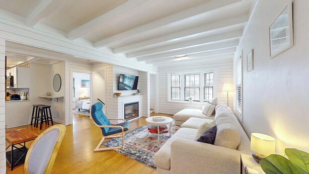 A spacious living room with a fireplace, a television mounted above it, and a large window with blinds.