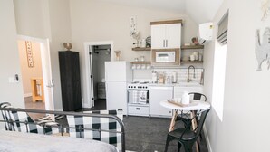 A compact kitchen with a refrigerator, stove, microwave, and sink. There is a dining area with a table and chairs. - Barn  Stay (Hurricane)