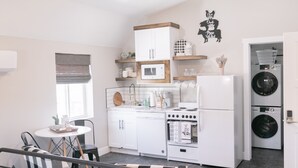 A compact kitchen with white cabinets, a stove, and a microwave. There is a ceiling fan and a window with blinds. - Barn  Stay (Hurricane)