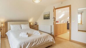 A bedroom with a bed, bedside tables, a radiator, a wooden door leading to a bathroom, and a ceiling light.