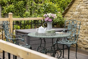 Une table ronde avec une théière blanche et des tasses, un vase rempli de fleurs et deux chaises ornées de motifs floraux.