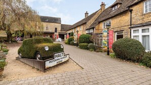 Une charmante rue de village où sont exposées des voitures anciennes, avec une pancarte indiquant : « MUSÉE DES AUTOMOBILES, À QUELQUES PAS ».