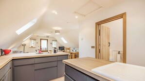A modern kitchen with a central island, a dining area with a wooden table, and a large window providing natural light.