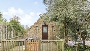 A stone cottage with a wooden deck, a small table and chairs, and a wooden fence.