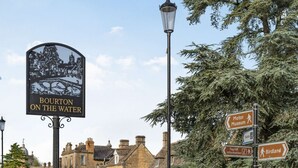 Un panneau indiquant « Bourton-on-the-Water », avec des panneaux directionnels vers le « musée automobile », les « toilettes », l'« office de tourisme » et le « parc ornithologique ».
