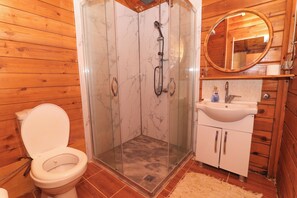 A wooden cabin bathroom with a glass-enclosed shower, a toilet, and a sink with a mirror above it. - Demre Sahildeki Ev Bungalov (Demre)