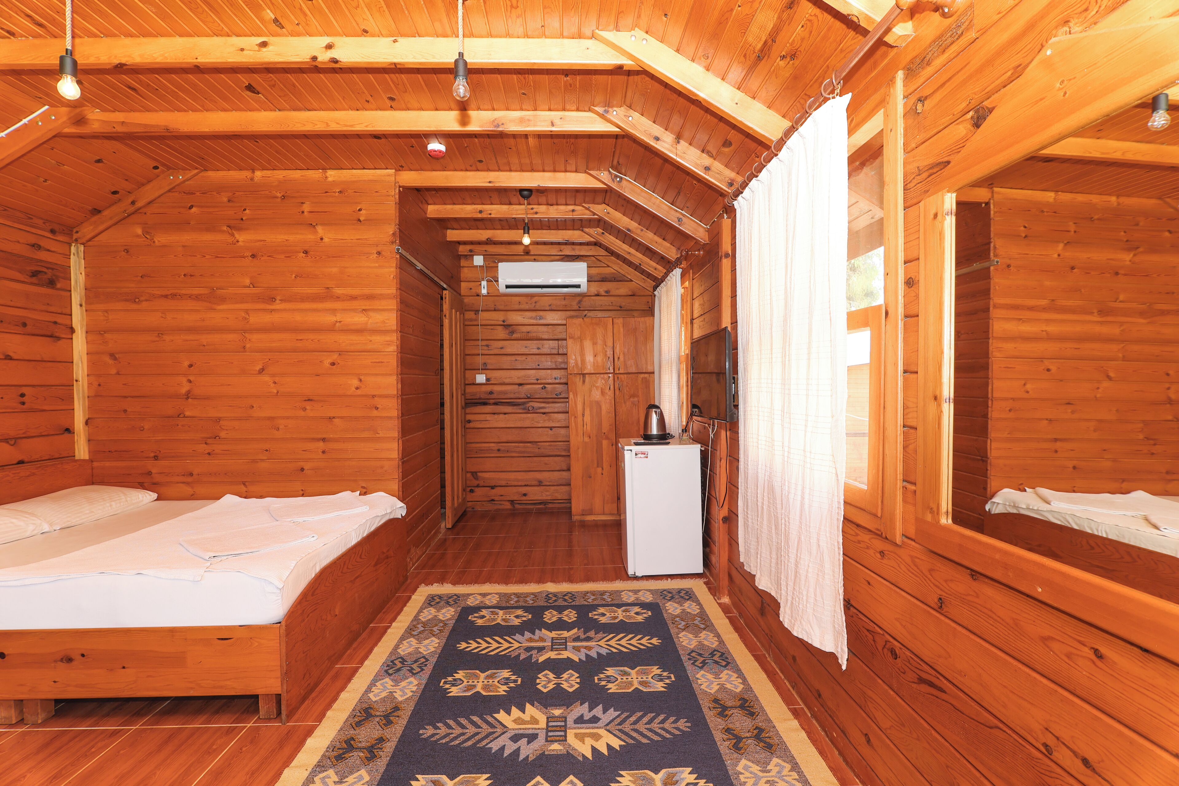 Una habitación tipo cabaña de madera con dos camas, un refrigerador pequeño y techo de madera.