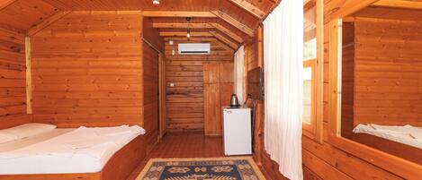Una habitación tipo cabaña de madera con dos camas, un refrigerador pequeño y techo de madera.