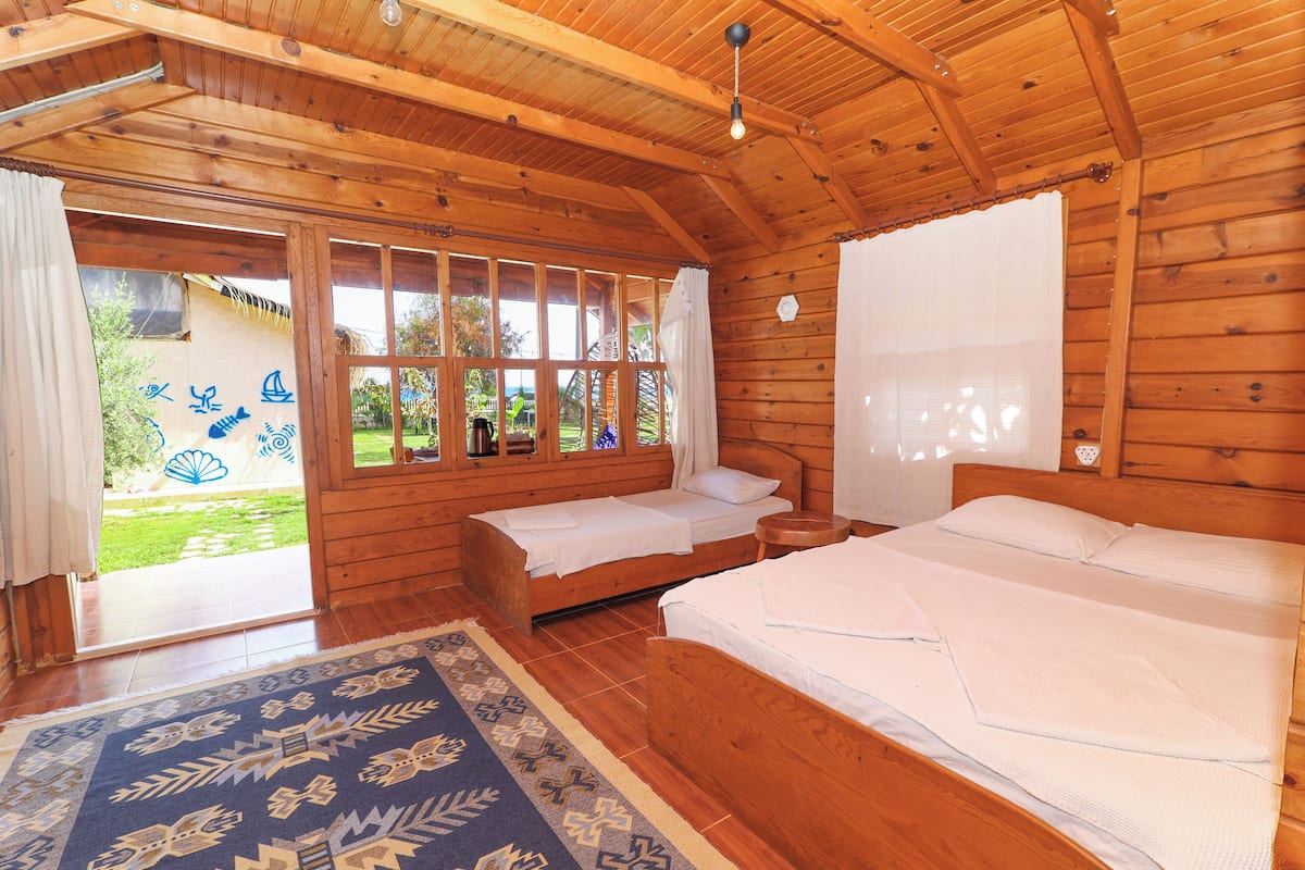 A wooden cabin with two beds, a large window, and a view of the outdoors.