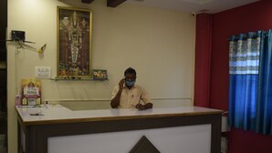 Una reception con un quadro sacro incorniciato sopra, una piccola mensola con oggetti e una parete rossa con una tenda blu.