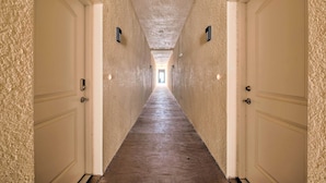 Um corredor comprido e estreito, com portas brancas de ambos os lados e piso de madeira.