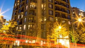 Un immeuble de grande hauteur doté de nombreux balcons et fenêtres, entouré d’arbres et de lampadaires.