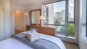 Une chambre moderne avec un grand lit, une commode en bois, un miroir et une fenêtre donnant sur la ville.