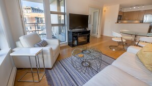 Un salon moderne avec un canapé, une table basse et un téléviseur. Il y a également un coin cuisine avec une table à manger et des chaises.