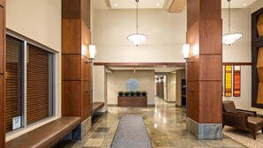 Un hall d’hôtel doté d’un comptoir d’accueil central, d’espaces aménagés avec des sièges et d’un mur décoratif orné d’un motif circulaire.