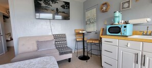 Un espace de vie compact comprenant un canapé, deux tabourets de bar, un four à micro-ondes et un petit coin cuisine.