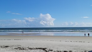Une plage avec une vaste étendue de sable, une mer calme et quelques personnes qui se promènent.