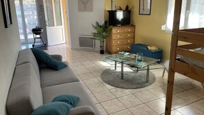 Una sala de estar con un sofá, una mesa de centro de vidrio, un aparador de madera y una televisión.