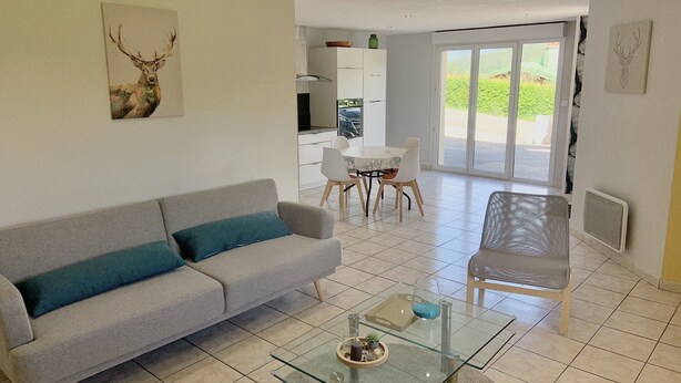 Una sala de estar moderna con un sofá gris, una mesa de centro de vidrio y una zona de comedor con una mesa y sillas blancas.