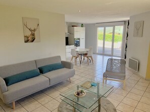 A modern living room with a grey sofa, a glass coffee table, and a dining area with a white table and chairs.