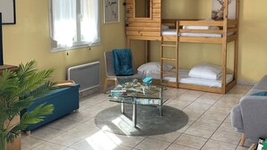 Una habitación con literas, una mesa de vidrio, un sofá azul y una planta en maceta.