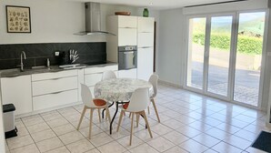Una cocina moderna con armarios blancos, una campana de acero inoxidable y una encimera negra. Se observa una mesa de comedor con cuatro sillas y una ventana que ofrece vistas a zonas verdes.