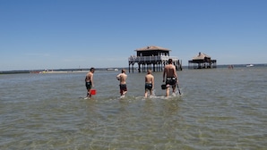 Eine Strandansicht mit klarem Wasser, Holzbauten und Menschen.