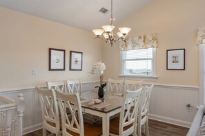 A dining room with a round table, white chairs, a chandelier, and framed pictures on the walls.