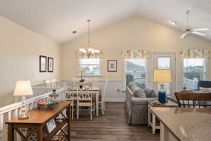 A spacious kitchen with a dining area, a ceiling fan, and large windows with floral curtains.