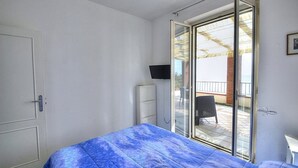 Une chambre avec un lit, une télévision, une porte-fenêtre coulissante donnant sur un balcon et une chaise à l’extérieur.
