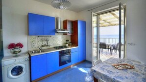 Une cuisine compacte avec des meubles bleus, un lave-linge et un coin repas avec une table dressée pour deux personnes.