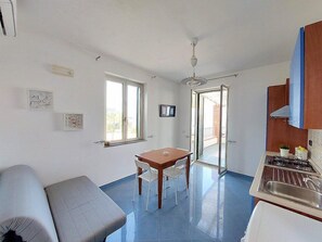 A compact kitchen with a dining area, a sofa, and a ceiling fan.
