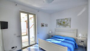 A bedroom with a bed, a TV, a sliding glass door, and a small table. - Casa Terry B: A graceful apartment located right on the beach, with Free WI-FI. (Castellabate)