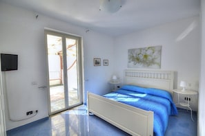 A bedroom with a bed, a TV, a sliding glass door, and a small table.