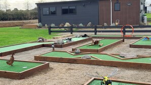 Un parcours de mini-golf avec des trous numérotés, une structure en bois portant l’inscription « Peachy », et un petit bâtiment en arrière-plan.