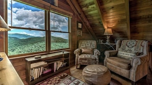 A cozy cabin interior with a large window offering a view of a forested mountain range. - Top of the Ridge Chalet - Pet Friendly | Mountain Views | Hot Tub | Multiple Decks (Blue Ridge)