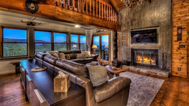A spacious living room with a large leather sectional sofa, a fireplace, and large windows offering a view of the mountains. - Top of the Ridge Chalet - Pet Friendly | Mountain Views | Hot Tub | Multiple Decks (Blue Ridge)