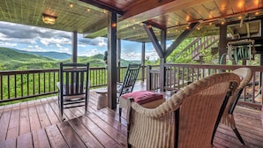 A wooden deck with wicker chairs and a table, overlooking a mountainous landscape. - Top of the Ridge Chalet - Pet Friendly | Mountain Views | Hot Tub | Multiple Decks (Blue Ridge)