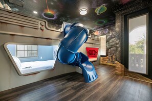 Una habitación con un diseño de cama único, techo con temática galáctica y vistas a través de un gran ventanal.