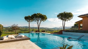 Piscina com vista para colinas e árvores, área de estar externa e espaço coberto.