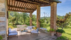 A covered outdoor seating area with brick pillars, white cushioned chairs, and a table set for dining. - Podere Pratovecchio 14 2 (Torrita di Siena)