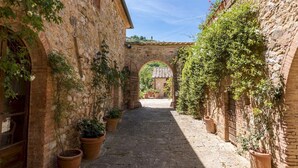 A narrow stone alleyway with potted plants and an archway leading to a building. - Podere Pratovecchio 14 2 (Torrita di Siena)