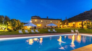 A swimming pool with lounge chairs and umbrellas, a large building with multiple windows, and a well-maintained lawn. - Podere Pratovecchio 14 2 (Torrita di Siena)