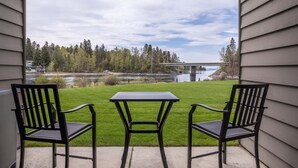 Un patio con dos sillas y una mesa, con vistas a un área verde, un puente y una masa de agua.