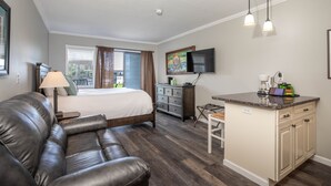 Habitación de hotel con cama, sofá de cuero, kitchenette pequeña, televisor y ventana con cortinas.