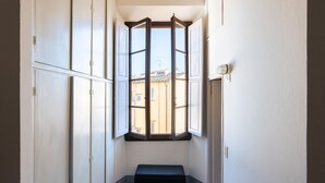 A narrow hallway with a bench at the end, a large window with a view of buildings outside, and white walls. - Borgo Santa Croce in Firenze (Florence)