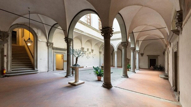 A spacious interior with high ceilings, arched columns, and a central staircase. - Borgo Santa Croce in Firenze (Florence)