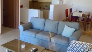 A living room with a sofa, a coffee table, and a dining area with chairs and a table. - Romanza Villas (Sitia)