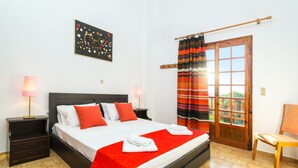 A neatly made bed with a red blanket, two bedside lamps, a wooden chair, and a door with a striped curtain. - Romanza Villas (Sitia)