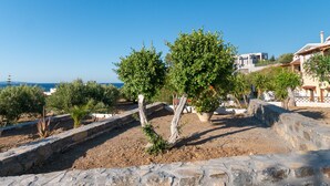 A stone wall with a tree in the foreground, a clear blue sky, and buildings in the background. - Romanza Villas (Sitia)